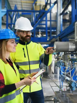 Man and woman wearing high vis clothing and hard hars, inspecting a piece of machinery in a water plant